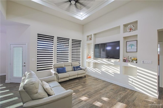 living room with hardwood / wood-style flooring, a towering ceiling, built in features, and ceiling fan