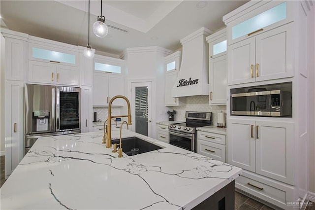 kitchen featuring sink, custom exhaust hood, appliances with stainless steel finishes, pendant lighting, and white cabinets