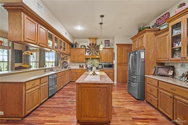 kitchen with a kitchen island, light wood-type flooring, decorative light fixtures, and appliances with stainless steel finishes