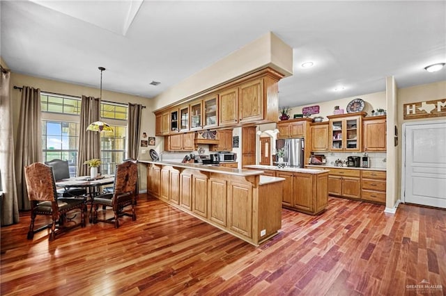 kitchen with pendant lighting, light wood-type flooring, kitchen peninsula, and stainless steel appliances