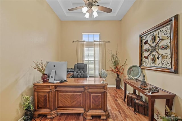 office space featuring ceiling fan, a raised ceiling, and light hardwood / wood-style flooring