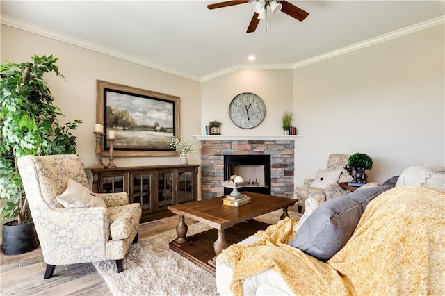 living room featuring ceiling fan, light hardwood / wood-style floors, a stone fireplace, and ornamental molding