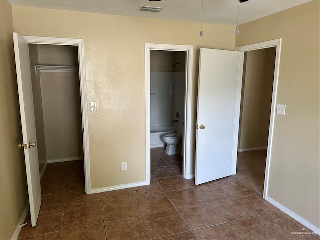 unfurnished bedroom with connected bathroom, dark tile patterned floors, and a closet