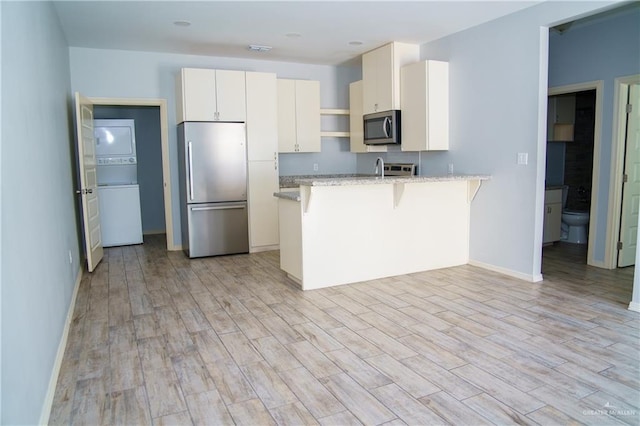 kitchen with a kitchen bar, kitchen peninsula, appliances with stainless steel finishes, and light hardwood / wood-style flooring