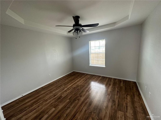 unfurnished room with dark hardwood / wood-style flooring, a raised ceiling, and ceiling fan