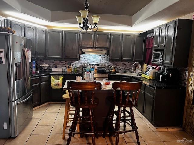 kitchen with decorative backsplash, light tile patterned floors, a tray ceiling, stainless steel appliances, and dark brown cabinets