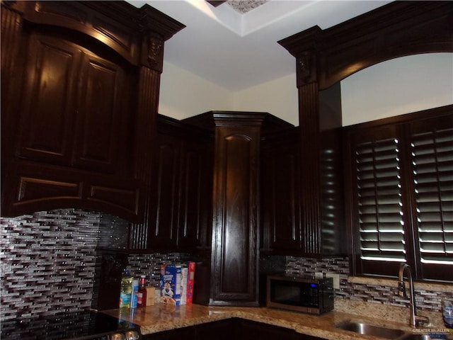 kitchen featuring light stone countertops, dark brown cabinets, backsplash, and sink