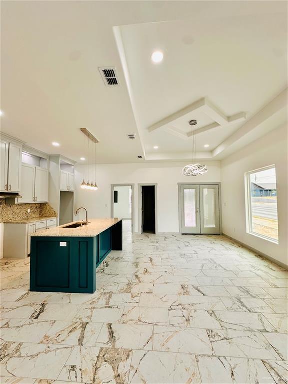 kitchen with a center island with sink, white cabinetry, hanging light fixtures, and sink