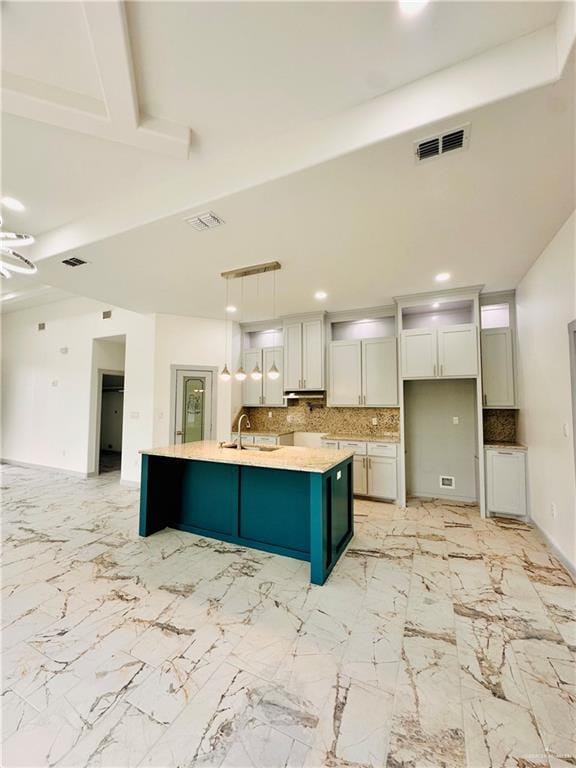 kitchen with pendant lighting, a kitchen island with sink, white cabinets, sink, and tasteful backsplash