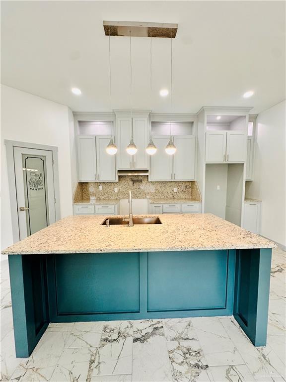 kitchen with a large island, sink, hanging light fixtures, light stone counters, and white cabinets