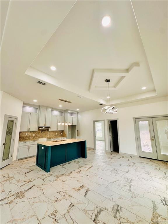 kitchen featuring pendant lighting, white cabinets, sink, an island with sink, and a tray ceiling