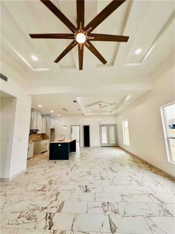 unfurnished living room with ceiling fan, beam ceiling, sink, and a tray ceiling