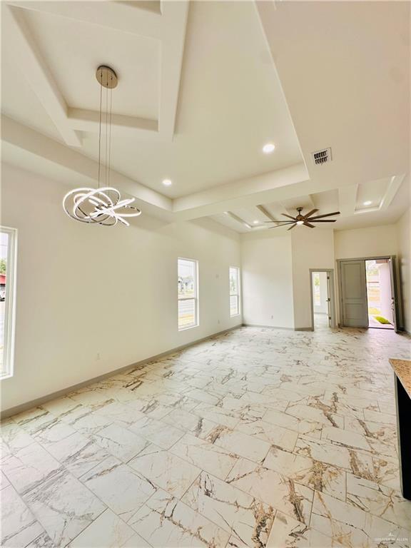 empty room featuring ceiling fan with notable chandelier, a raised ceiling, and a healthy amount of sunlight