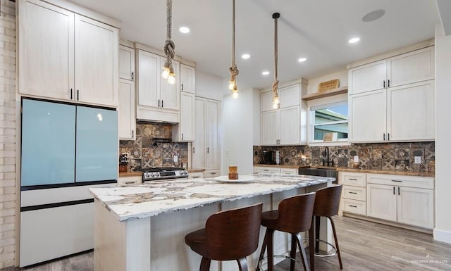 kitchen featuring gas range, light stone countertops, fridge, a kitchen island, and white cabinetry