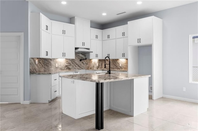 kitchen featuring white cabinetry, light stone counters, sink, and a center island with sink