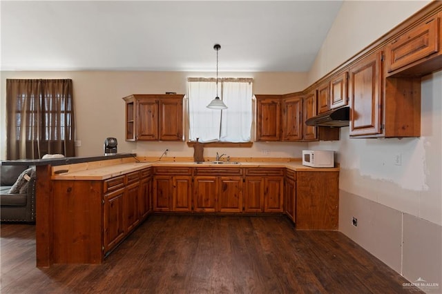 kitchen featuring kitchen peninsula, vaulted ceiling, sink, decorative light fixtures, and dark hardwood / wood-style floors