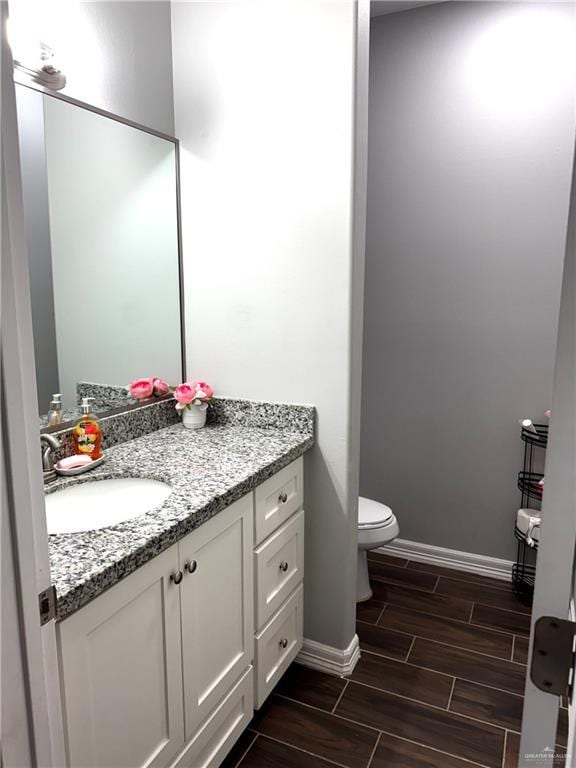 half bathroom featuring wood tiled floor, toilet, vanity, and baseboards