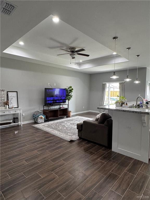 living area featuring baseboards, visible vents, a raised ceiling, and wood finish floors