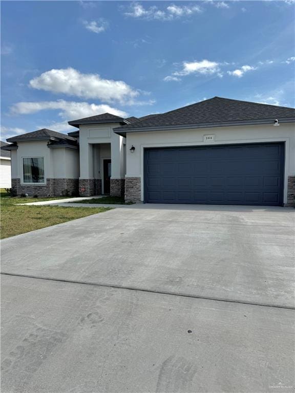 prairie-style house with a front yard, concrete driveway, an attached garage, and stucco siding