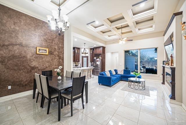 dining area with ceiling fan with notable chandelier, beamed ceiling, a high ceiling, coffered ceiling, and crown molding