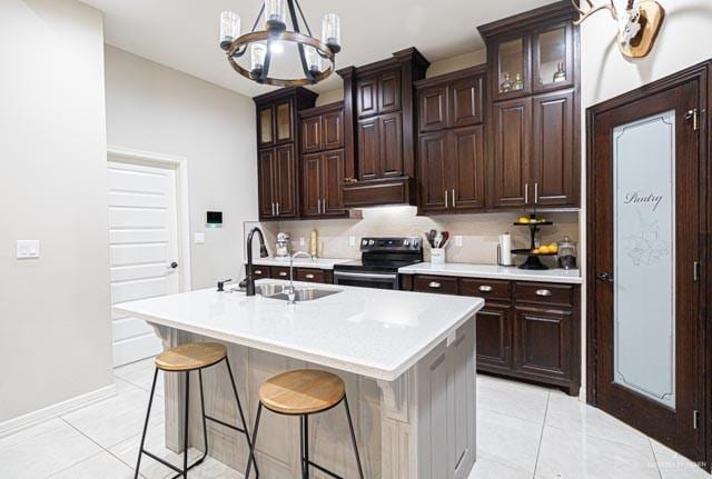 kitchen with dark brown cabinetry, sink, a center island with sink, light tile patterned floors, and electric stove