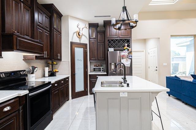 kitchen with appliances with stainless steel finishes, tasteful backsplash, sink, hanging light fixtures, and a kitchen island with sink