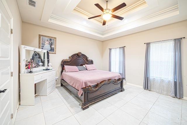 bedroom with ceiling fan, ornamental molding, a raised ceiling, and light tile patterned floors