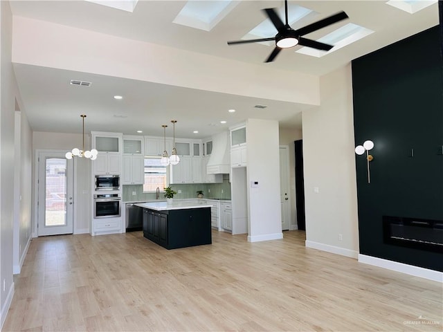 kitchen with stainless steel appliances, custom range hood, white cabinetry, a kitchen island, and ceiling fan with notable chandelier