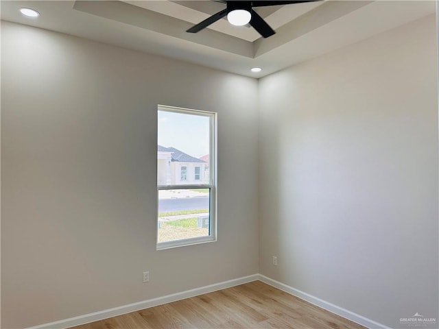 empty room with a tray ceiling, recessed lighting, a ceiling fan, light wood-type flooring, and baseboards