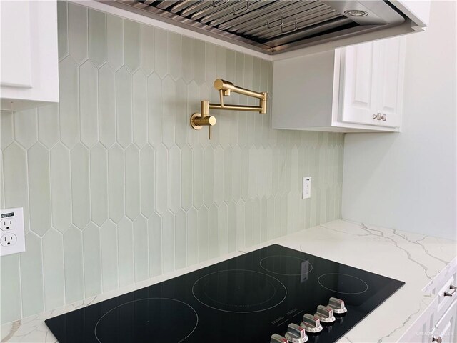 kitchen with custom range hood, black electric stovetop, white cabinets, and light stone counters