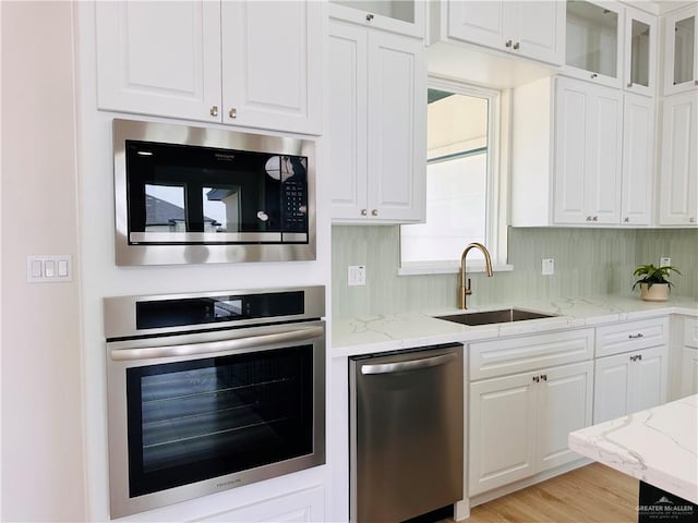 kitchen featuring light stone counters, white cabinetry, stainless steel appliances, and a sink