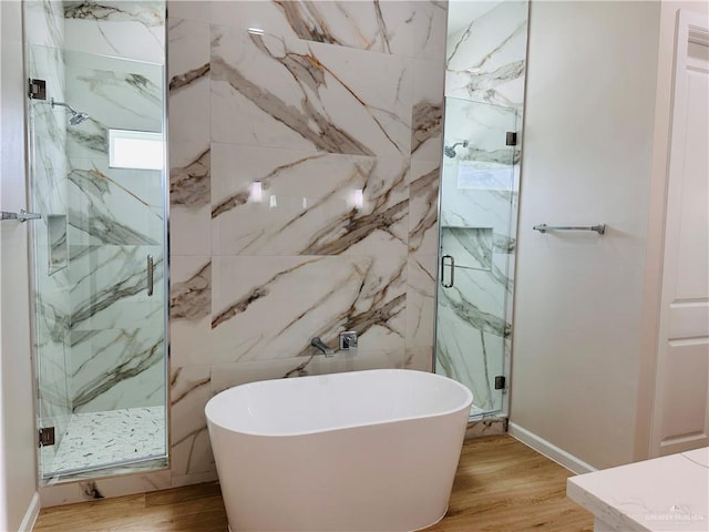 full bathroom featuring a freestanding tub, a marble finish shower, and wood finished floors