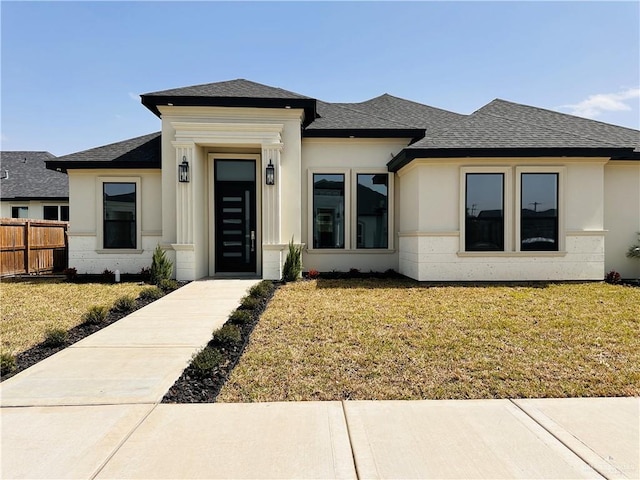 prairie-style home with stucco siding, a shingled roof, fence, and a front yard