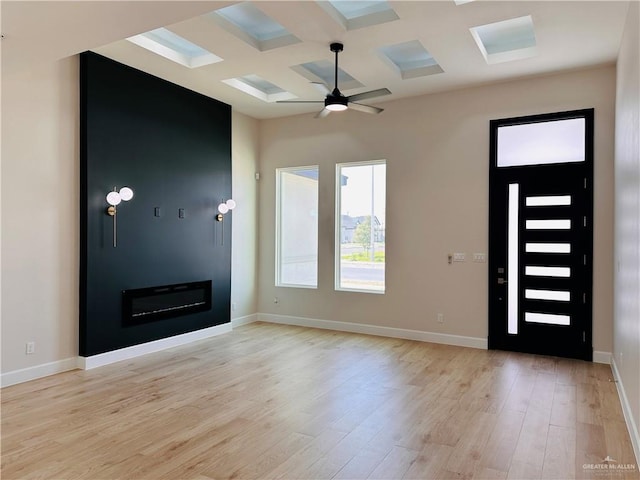 entryway featuring a large fireplace, coffered ceiling, baseboards, and light wood finished floors