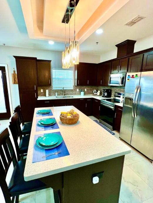 kitchen with hanging light fixtures, stainless steel appliances, a kitchen breakfast bar, tasteful backsplash, and a kitchen island