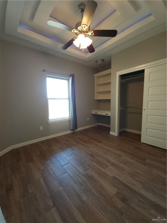 unfurnished bedroom with ceiling fan, dark hardwood / wood-style flooring, a raised ceiling, and a closet