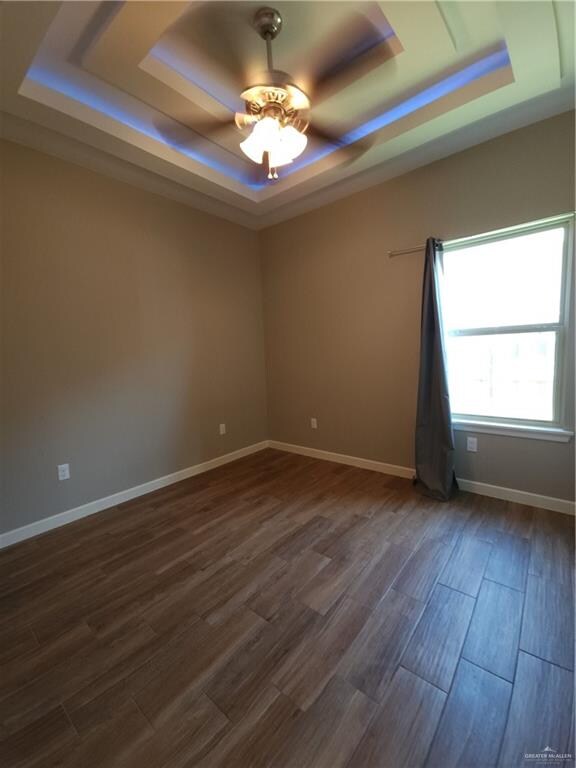 unfurnished room featuring a raised ceiling, dark wood-type flooring, and ceiling fan