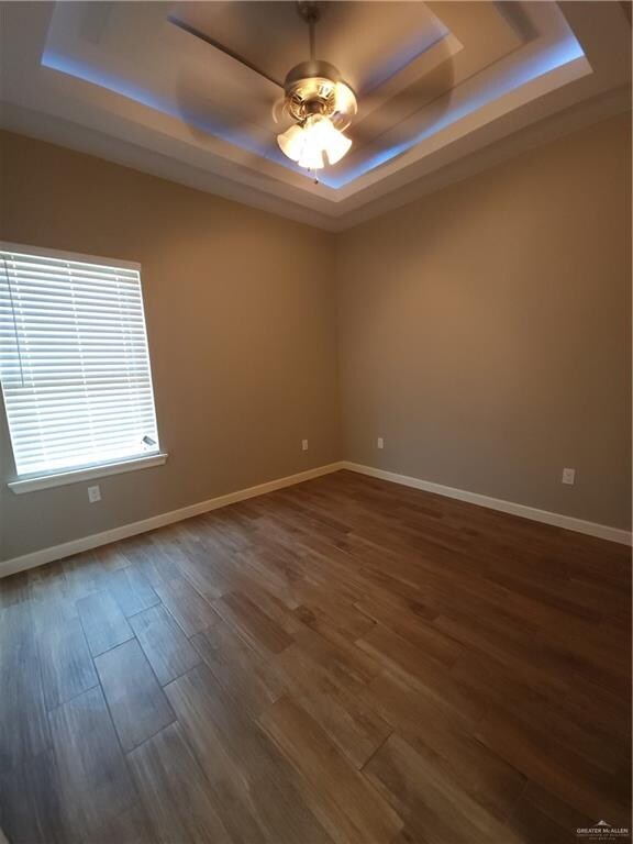 unfurnished room featuring ceiling fan, dark hardwood / wood-style flooring, and a raised ceiling