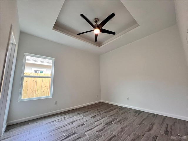 unfurnished room featuring ceiling fan, baseboards, wood finished floors, and a raised ceiling
