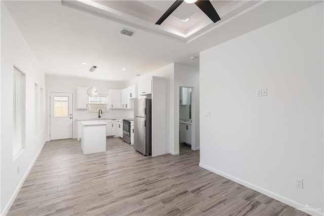 unfurnished living room featuring a ceiling fan, light wood-type flooring, a raised ceiling, baseboards, and visible vents