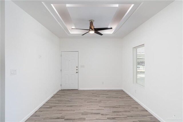 spare room featuring ceiling fan, baseboards, light wood-style floors, and a raised ceiling