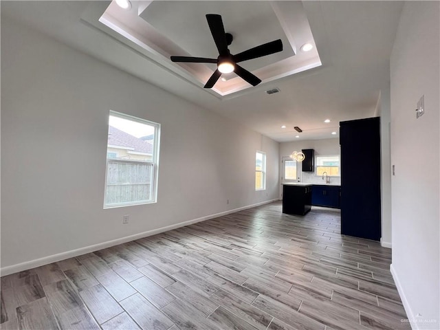 unfurnished living room featuring a tray ceiling, light wood-type flooring, baseboards, visible vents, and ceiling fan