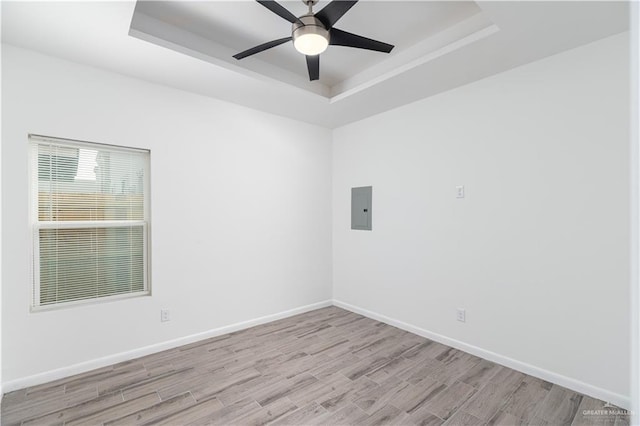unfurnished room with electric panel, a tray ceiling, light wood-type flooring, baseboards, and a ceiling fan