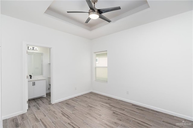 unfurnished bedroom featuring a raised ceiling, light wood-style flooring, and baseboards