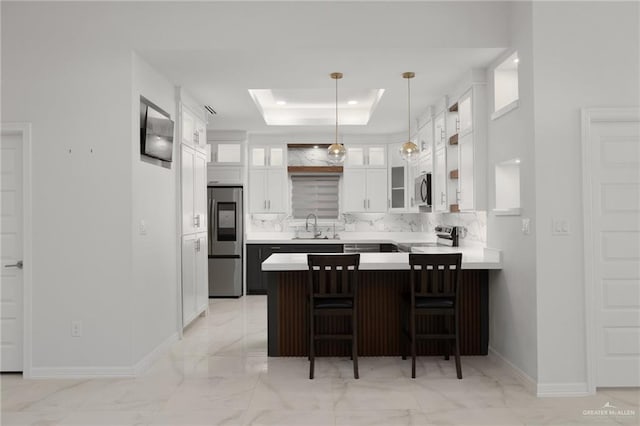 kitchen with a peninsula, a sink, stainless steel appliances, a raised ceiling, and marble finish floor