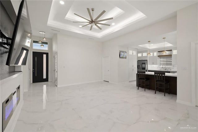 interior space featuring a tray ceiling, recessed lighting, baseboards, marble finish floor, and ceiling fan