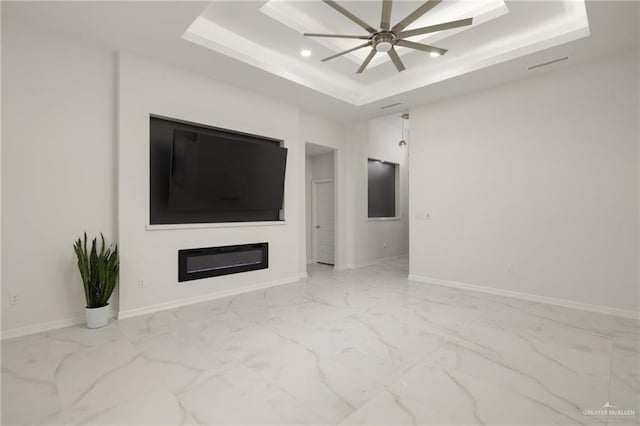 unfurnished living room with a tray ceiling, baseboards, and marble finish floor
