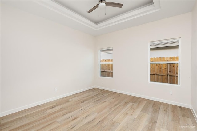 empty room featuring a raised ceiling, ceiling fan, and light hardwood / wood-style floors