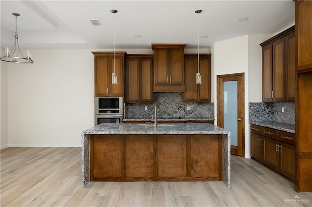 kitchen featuring light stone countertops, hanging light fixtures, and a kitchen island with sink