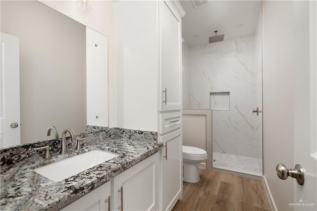 bathroom with vanity, toilet, wood-type flooring, and tiled shower